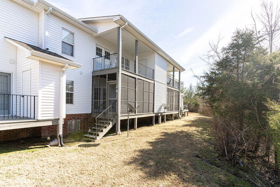 Side view of a two-story house with a raised porch and screened-in balcony.