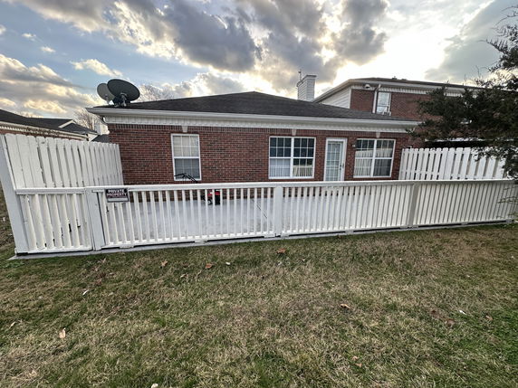 Front view of a brick house with a white fence and satellite dish on the roof.