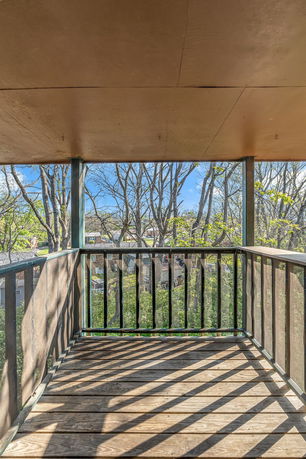 Wooden balcony with railing, providing a view of trees and a neighborhood.