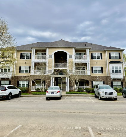 Front view of a multi-story apartment building with balconies and parking area.