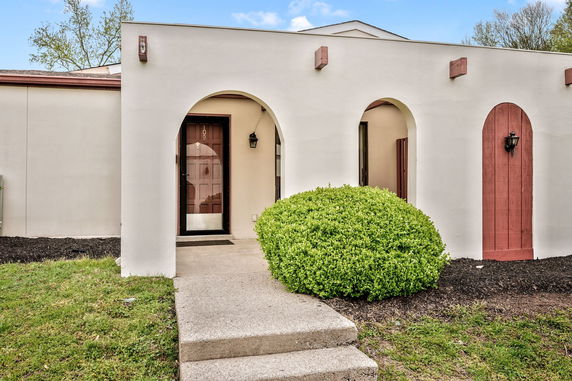 Front view of a house with arched doorways and a bush in front.