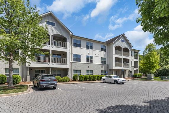 Front view of a three-story residential building with balconies and a parking area.