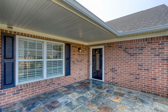 Front view of a brick house with large windows and a glass door under a covered porch.