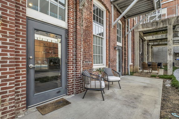 Front view of a building with exposed brick walls and a glass door entrance, featuring outdoor seating.