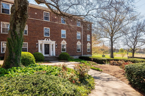 Front view of a three-story brick building with a central entrance and surrounding greenery.