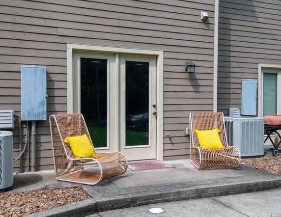 Back view of a house with patio chairs and air conditioning units.