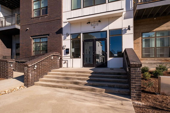 Front view of a modern building entrance with brick and white facade, featuring steps leading to glass doors.
