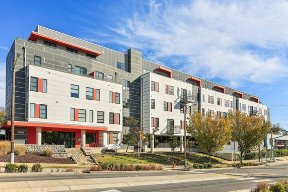 Front view of a modern multi-story apartment building with red accents and large windows.