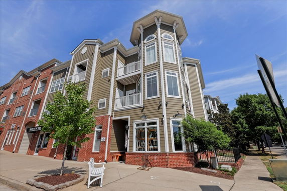 Front view of a mixed-use building with red brick and beige siding, featuring multiple balconies.