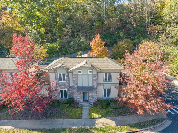 Front view of a two-story house with stone and siding exterior, surrounded by trees with autumn foliage.