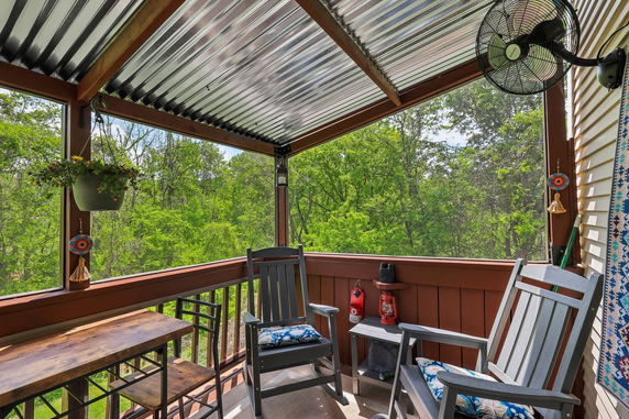 Covered outdoor seating area with rocking chairs and greenery visible beyond.