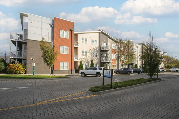 Front view of a modern multi-story apartment building with balconies and parking area.