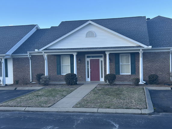Front view of a brick house with a covered entryway and red door.