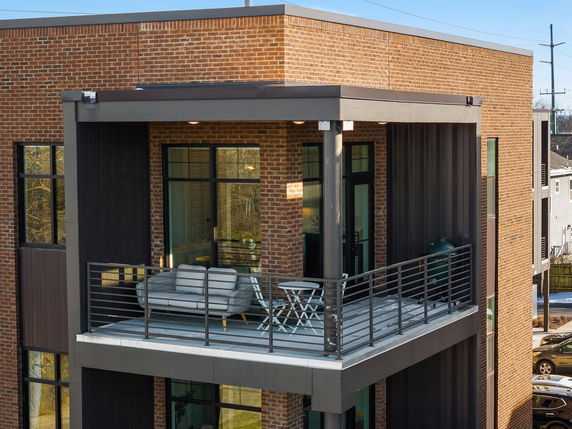 Front view of a modern brick building with a balcony featuring seating and a grill.