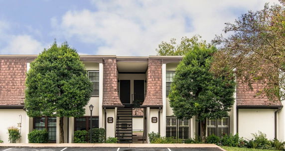 Front view of a two-story residential building with wooden roofing elements and windows.