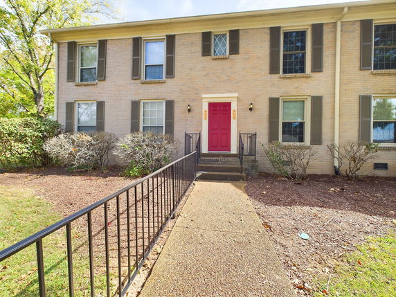 Front view of a two-story brick house with a red door and multiple windows.