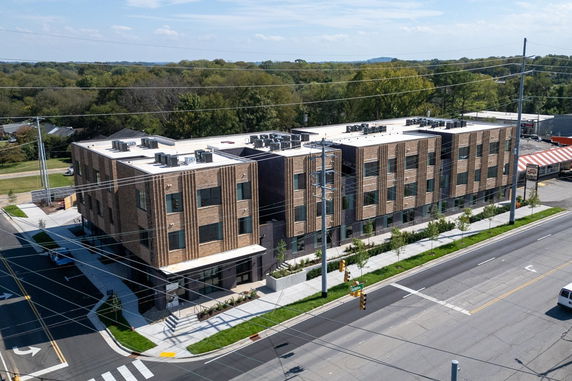 Aerial view of a three-story brick building with a flat roof, featuring multiple windows and rooftop units, located at a street corner.