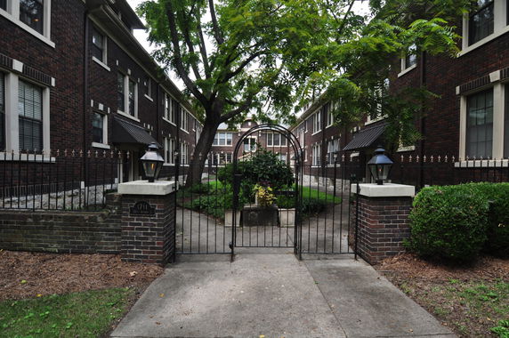 Front view of a multi-story brick apartment building with an entrance gate and pathway.