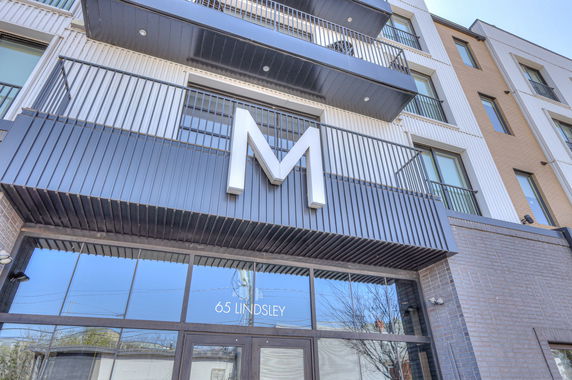 Front view of a modern multi-story building with balconies and large 'M' letter sign.
