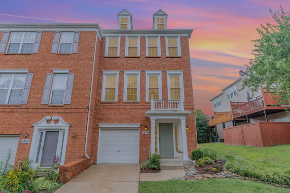 Front view of a three-story brick townhouse with a garage and small porch.