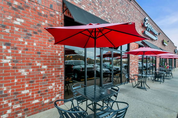 Front view of a brick building with outdoor seating and red umbrellas.