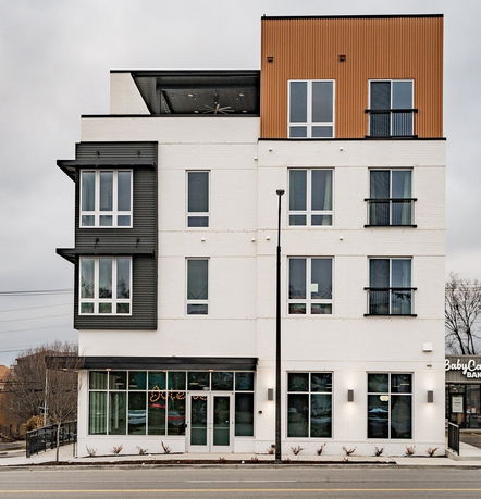 Front view of a modern multi-story building with large windows and a mix of white brick and colored paneling.