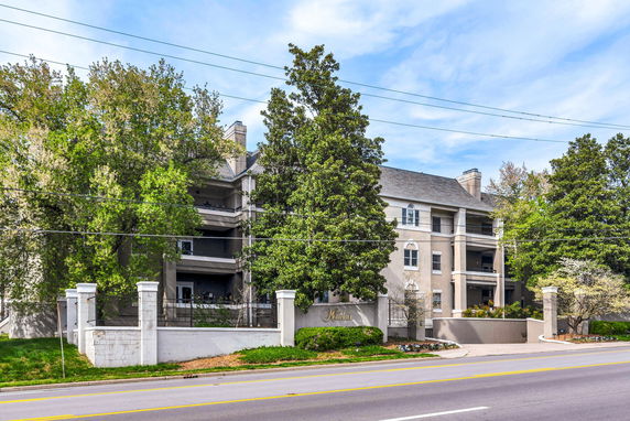 Front view of a multi-story residential building with trees and a driveway.