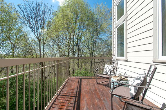 View from a balcony attached to a building with wooden decking and metal railing, overlooking trees.