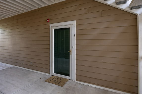 Front view of a building entrance with a glass door and brown siding.