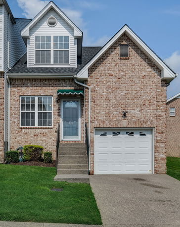 Front view of a brick house with a single garage and steps leading to the front door.