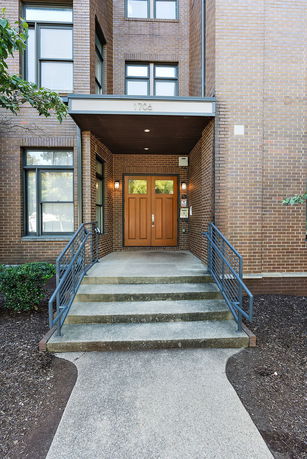 Front view of a brick building entrance with double wooden doors and metal railings.