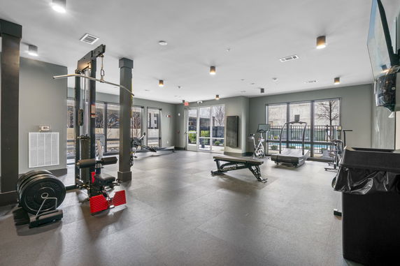 Interior view of a gym area with exercise equipment and large windows.
