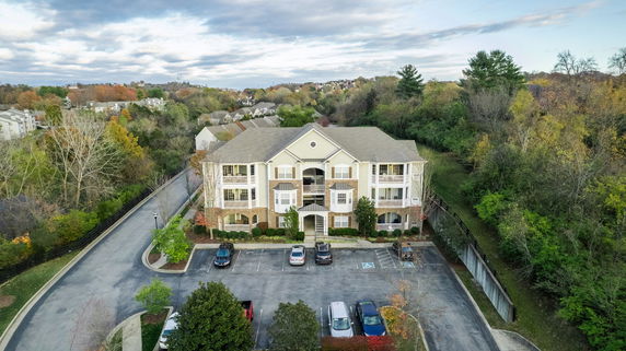 Front view of a multi-story residential building with parking area and surrounding trees.