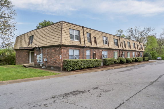 Front view of a two-story brick apartment building with multiple windows and a shingled roof.