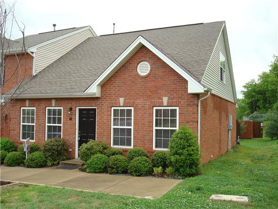 Front view of a brick single-story house with a black front door and symmetrical windows.
