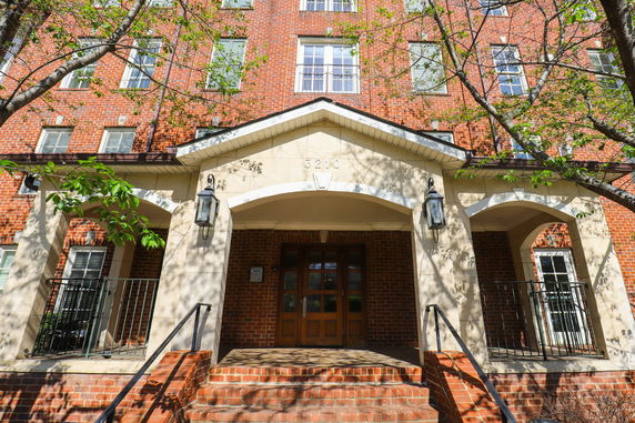 Front view of a multi-story brick building with a covered entrance and steps leading up.