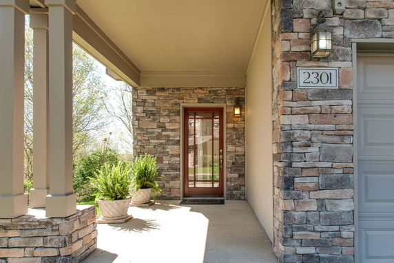 Front view of a stone exterior house entrance with a wooden door and outdoor lighting.