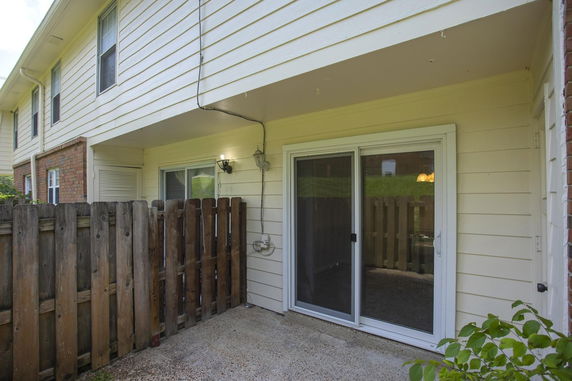 Rear view of a two-story house with sliding glass doors and wooden fencing.