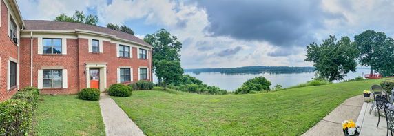 Panoramic view showing a two-story brick building with a scenic view of a lake and trees in the background.