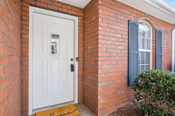 Front view of a red brick house with a white door and window with shutters.