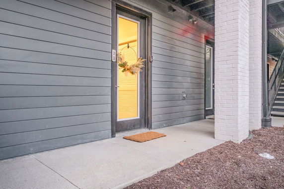 Front view of a building entrance with a glass door and gray siding.