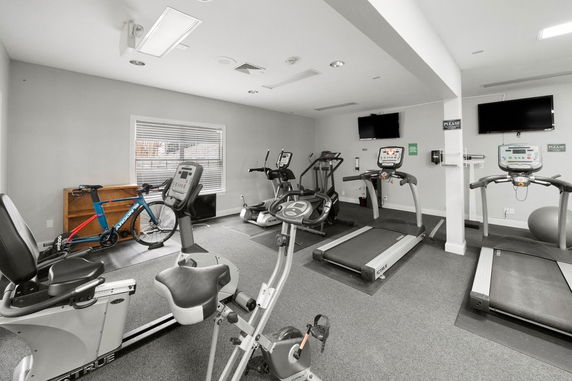 Room with exercise equipment including treadmills and stationary bikes.
