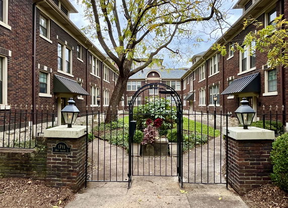 Front view of a two-story brick building with an arched gate and landscaped courtyard.