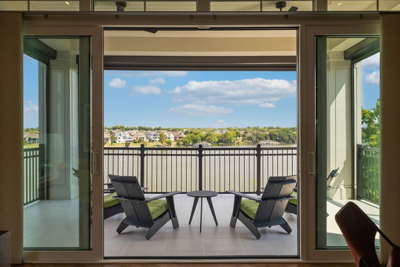 View of a balcony with chairs facing towards a water body and houses in the distance.