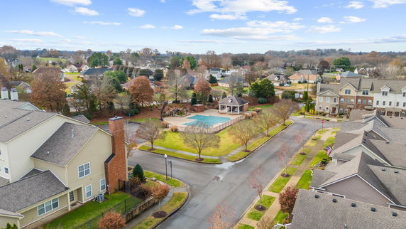 Wide aerial view of a residential neighborhood with houses, trees, and a swimming pool.