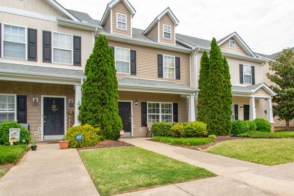 Front view of a row of townhouses with a front porch and shrubs.