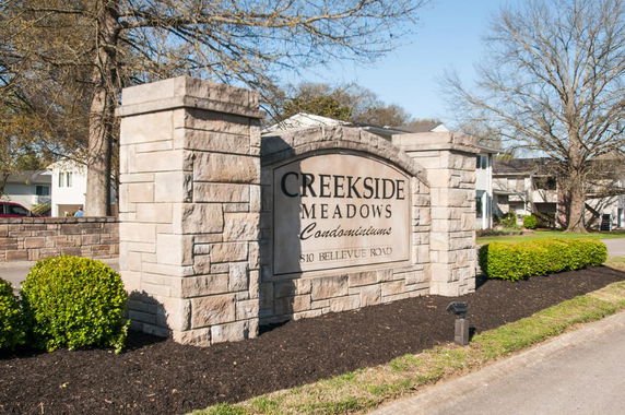 Front view of a stone entrance sign for Creekside Meadows Condominiums with buildings partially visible in the background.