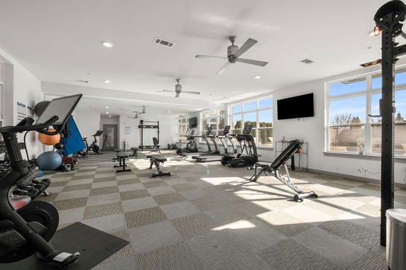 Interior of a bright gym room with exercise equipment and large windows.