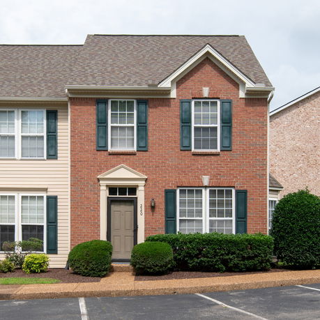 Front view of a two-story house with a brick facade and dark shutters.