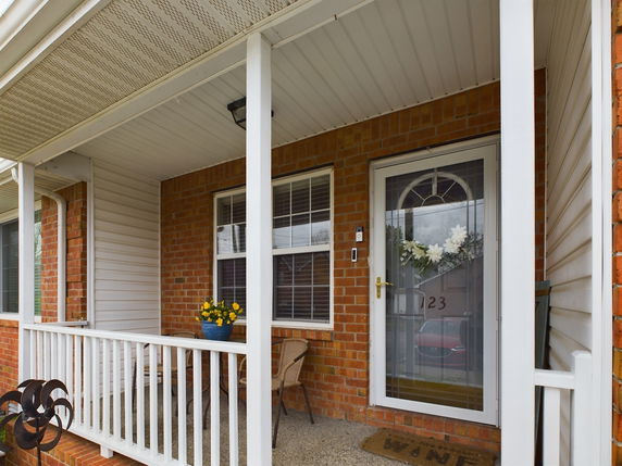 Front porch view of a brick house with white railings and a glass storm door.